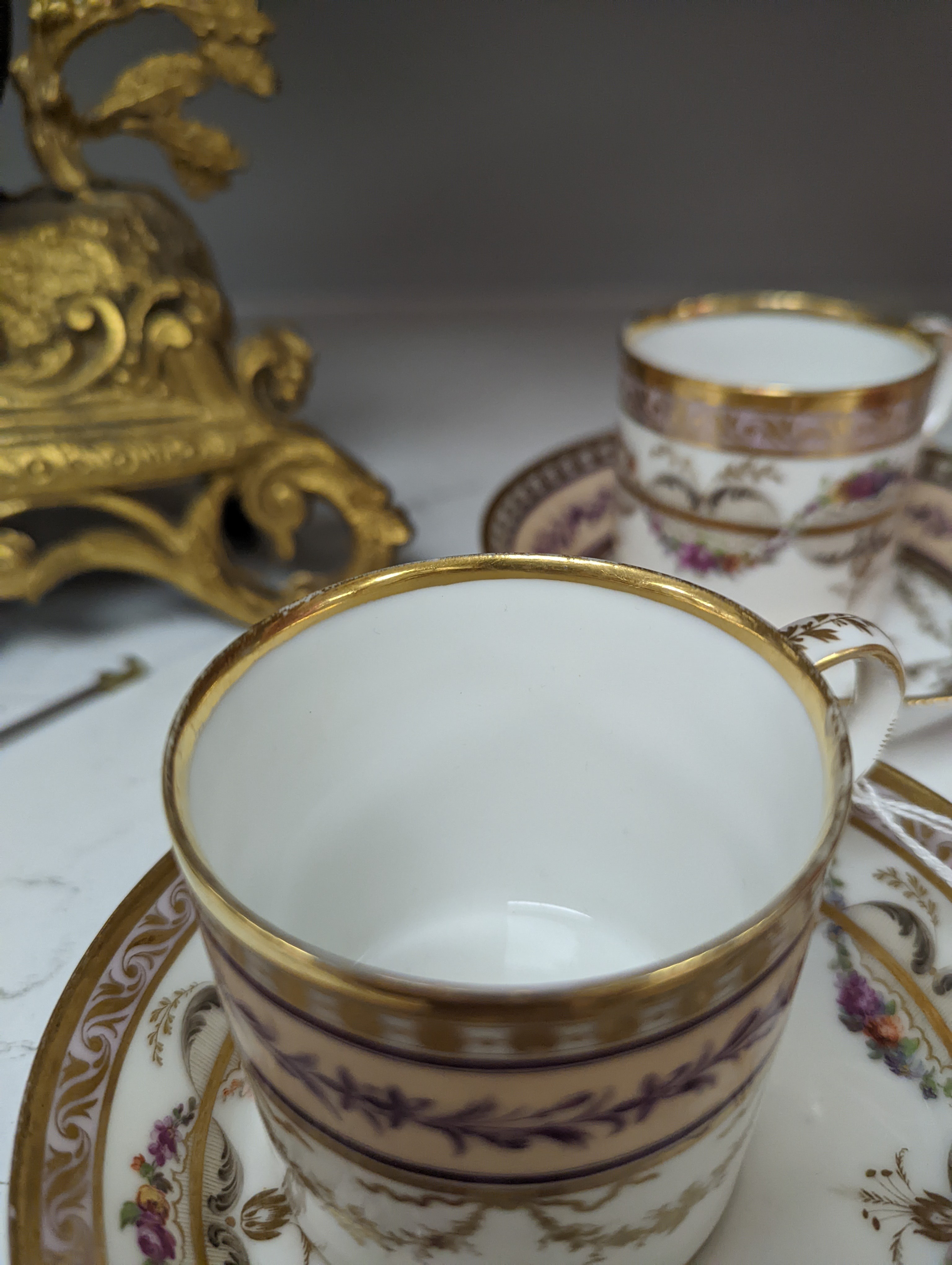 A Duc d'Angouleme coffee can and saucer painted with a puce chain of leaves on a salmon coloured ground and another painted with a flower chain, black feather and a gilt line, latter with stencilled red mark 'Manuf de M